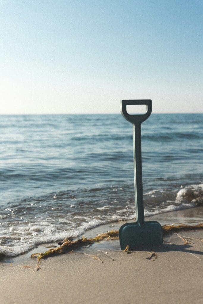 En mørkegrøn plastikskovl i sandet på en strand, som symboliserer det første spadestik i konceptudvikling og ingeniørrådgivning hos Phidan Engineering.
