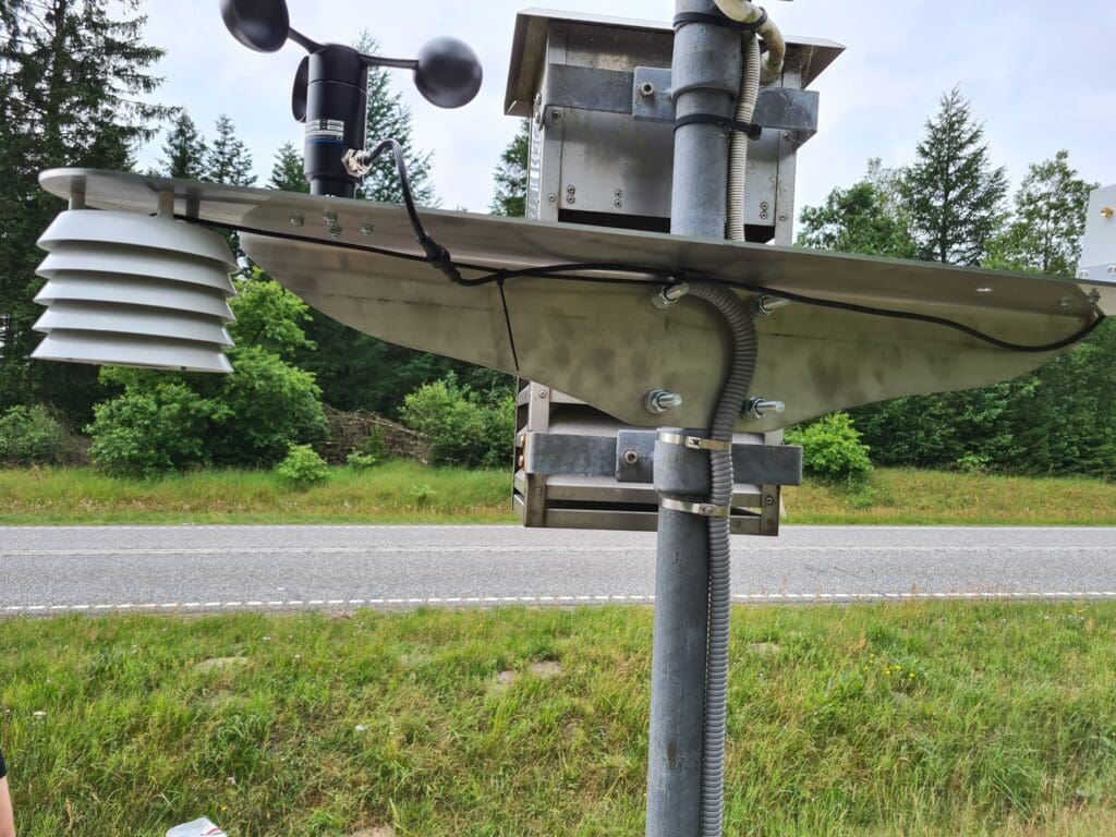 Professionel vejrstation monteret ved en vej med vindmåler og strålingsskjold til temperaturmåling, udviklet af Phidan Engineering.