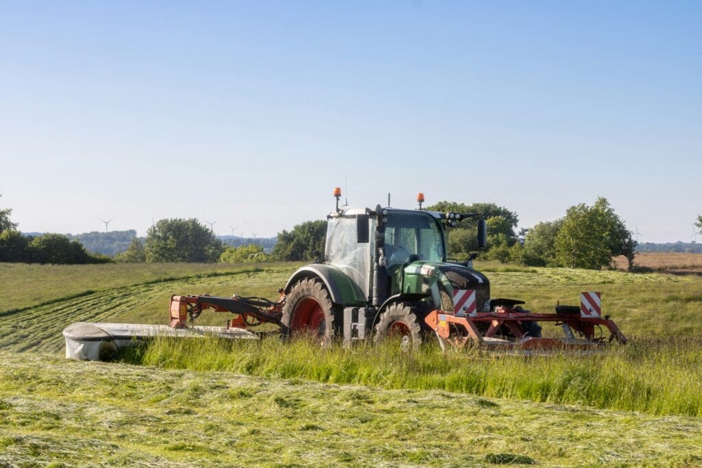 Grøn traktor med avanceret græsslåmaskine i arbejde på en mark – Phidan Engineering leverer ingeniørrådgivning til landbrugsmaskiner.