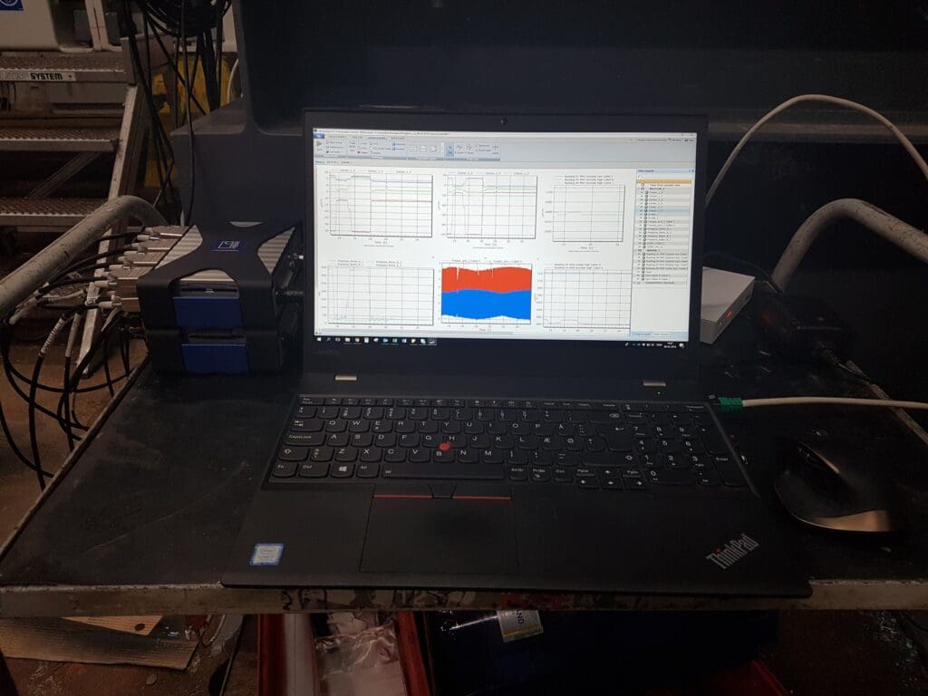 Professionel datalogning og testopsætning med en Lenovo ThinkPad og måleudstyr til indsamling af data fra strain gauges og sensorer i et industrielt miljø.
