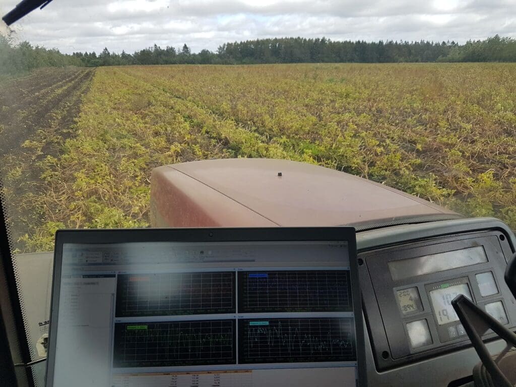 Laptop viser grafer for datalogning og fieldtest inde i en traktorkabine under arbejde i marken