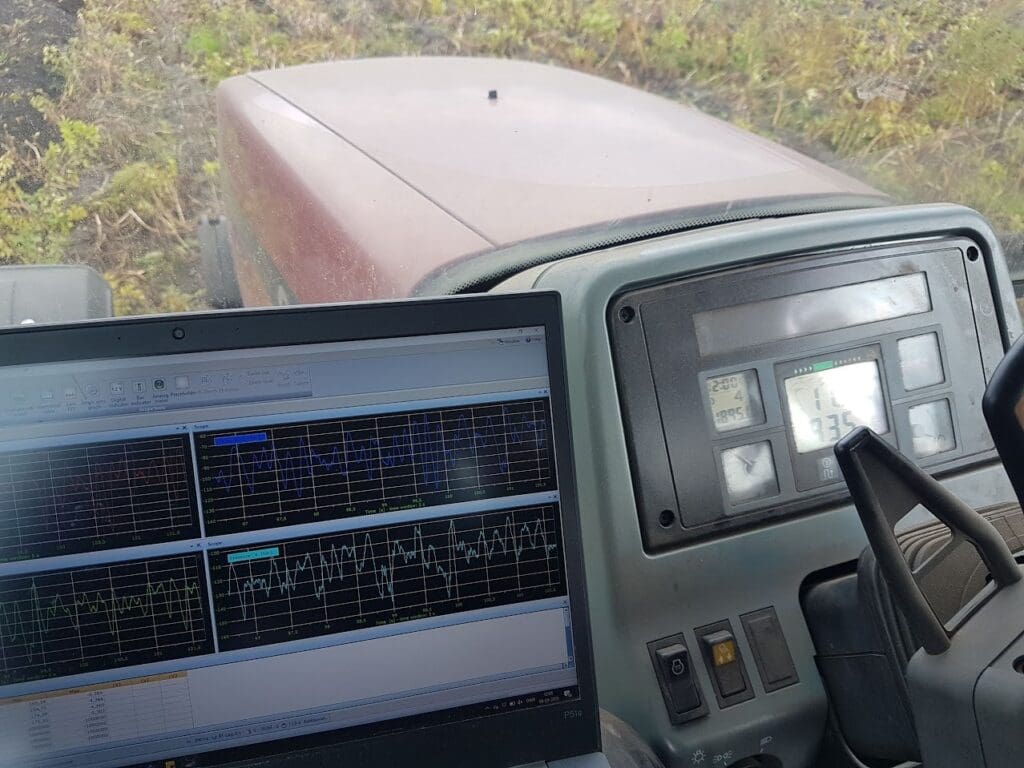 Laptop med grafer til vibrationstest og datalogning placeret i førerkabinen på en traktor under en marktest.