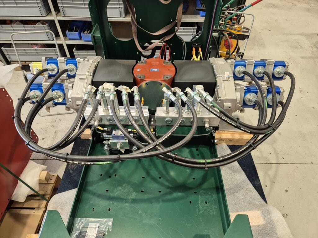 Et komplekst hydraulisk system med flere pumper, manifolds og hydraulikslanger monteret på en grøn stålramme i et værksted hos Phidan Engineering.