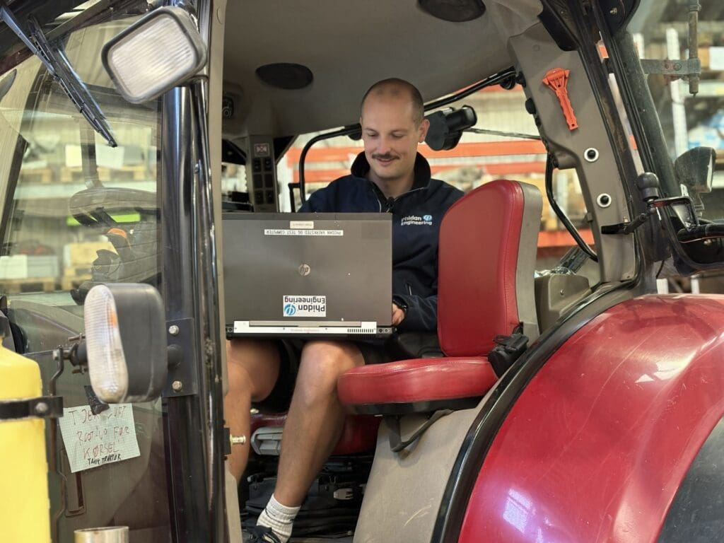 Ingeniør fra Phidan Engineering sidder i en traktor og arbejder med softwareudvikling og test af GPS-systemer via en bærbar computer.