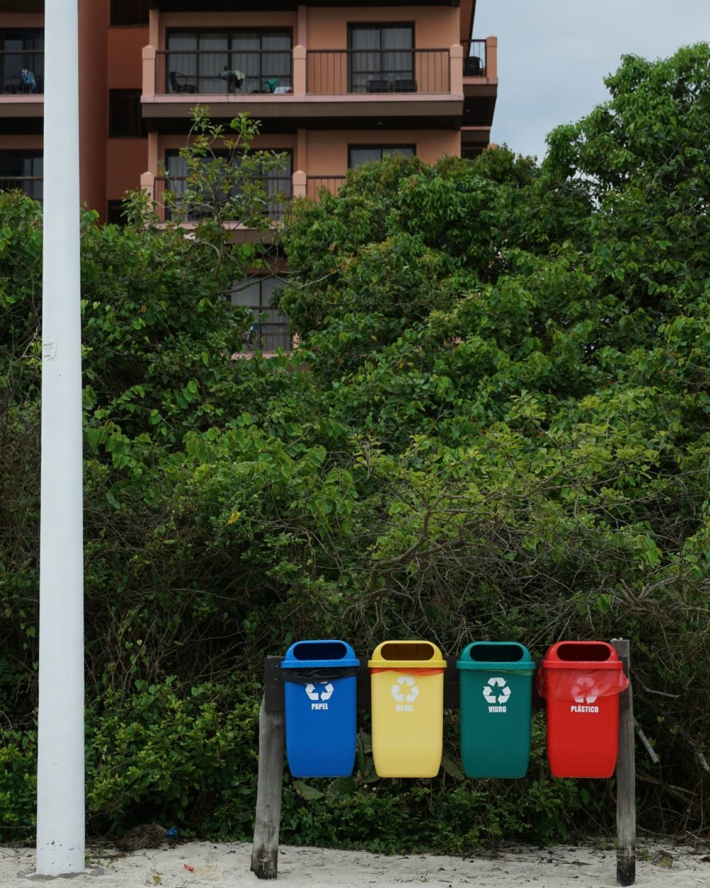 Phidan Engineering – Fokus på recycling og grøn omstilling Fire farverige affaldsbeholdere til sortering af papir, metal, glas og plast på en strand som symbol på recycling.