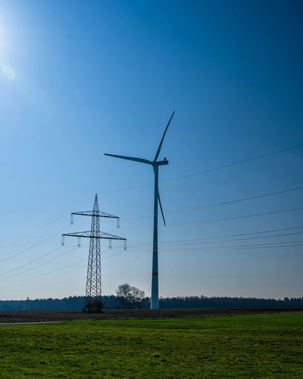 Ingeniørrådgivning og produktudvikling til energisektoren – Phidan Engineering En vindmølle og en elmast på en mark under en klar blå himmel, der repræsenterer Phidan Engineerings ekspertise inden for energi og teknisk infrastruktur.