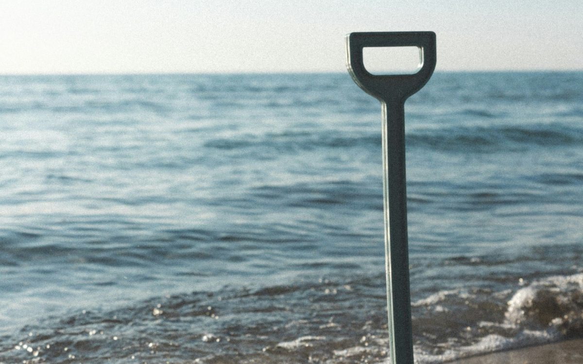 En mørkegrøn plastikskovl i sandet på en strand, som symboliserer det første spadestik i konceptudvikling og ingeniørrådgivning hos Phidan Engineering.
